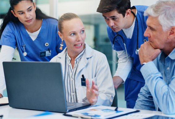 Woman, doctors and laptop with group at hospital with discussion for funding, management and review. People, leader and team with surgeon, problem solving and feedback with pc at wellness clinic
